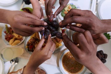 Dokunaklı bir yakın plan çekimde, Müslüman bir ailenin farklı elleri, kutsal Ramazan ayı boyunca orucun kırılışını sembolize ederek, kültürel birliğin bir anını yakalıyor.