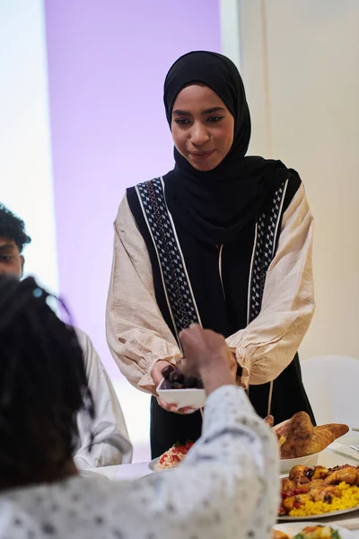 In a heartwarming scene during the sacred month of Ramadan, a traditional Muslim woman offers dates to her family gathered around the table, exemplifying the spirit of unity, generosity, and cultural