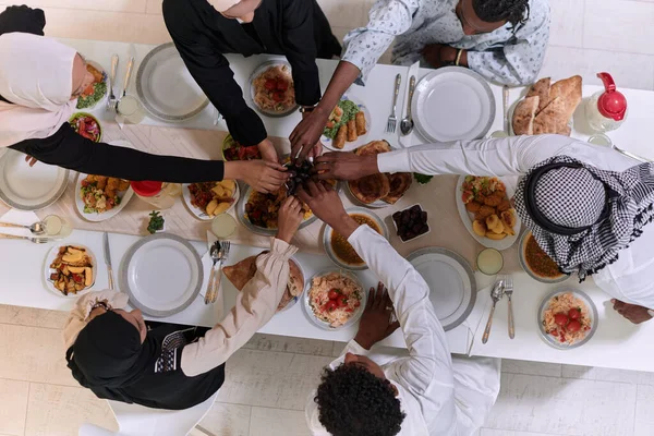 Top view of diverse hands of a Muslim family delicately grasp fresh dates, symbolizing the breaking of the fast during the holy month of Ramadan, capturing a moment of cultural unity, shared tradition