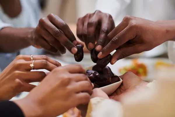 In a poignant close-up, the diverse hands of a Muslim family delicately grasp fresh dates, symbolizing the breaking of the fast during the holy month of Ramadan, capturing a moment of cultural unity