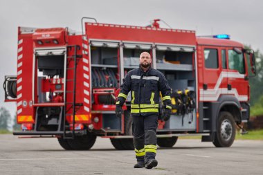 Sembolik olarak cesur bir itfaiyeci sarsılmaz bir cesaretle, azim ve liderliği simgeleyen bir adımla ilerlerken, arkasında itfaiye aracı itfaiye eylemleri için hazır bekliyor.