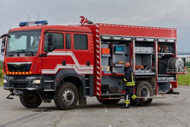 İtfaiyeci titizlikle modern bir itfaiye aracını tehlikeli durumlara müdahale ve boşaltma görevi için hazırlıyor. Yangına karşı güvenlik ve hazır olma azmini gösteriyor.