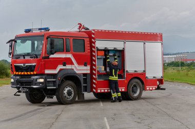 İtfaiyeci titizlikle modern bir itfaiye aracını tehlikeli durumlara müdahale ve boşaltma görevi için hazırlıyor. Yangına karşı güvenlik ve hazır olma azmini gösteriyor.