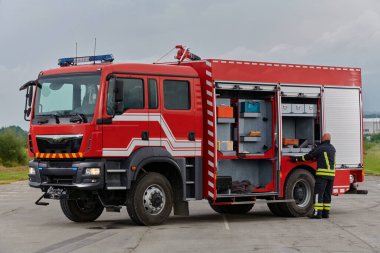 İtfaiyeci titizlikle modern bir itfaiye aracını tehlikeli durumlara müdahale ve boşaltma görevi için hazırlıyor. Yangına karşı güvenlik ve hazır olma azmini gösteriyor.