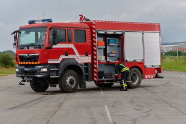 İtfaiyeci titizlikle modern bir itfaiye aracını tehlikeli durumlara müdahale ve boşaltma görevi için hazırlıyor. Yangına karşı güvenlik ve hazır olma azmini gösteriyor.