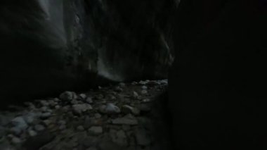 Antik bir mağaradan akan bir dereyle vahşi bir ormanda uçan insansız hava aracı görüntüsü.