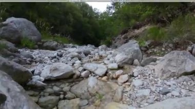 Antik bir mağaradan akan bir dereyle vahşi bir ormanda uçan insansız hava aracı görüntüsü.