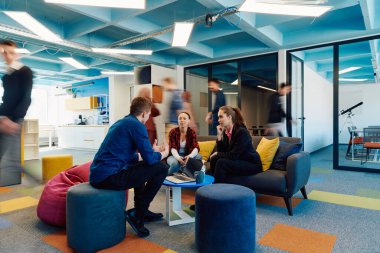 Çok ırklı bir girişim ekibi modern, açık alan çalışma ofisinde toplanıyor. Beyin fırtınası, dizüstü bilgisayarda çalışmak. Hareket bulanıklığı içinde dolaşan bir grup iş arkadaşı.