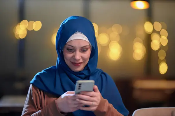 ヒジャーブで飾られた美しいヨーロッパのイスラム教徒の女性は 彼女の伝統と近代性のブレンドを体現し ラマダンの神聖な月にイフタールのために迅速に準備するために彼女のスマートフォンを使用します — ストック写真
