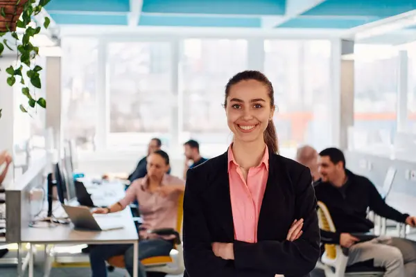 stock image Portrait of young smiling business woman in creative open space coworking startup office. Successful businesswoman standing in office with copyspace. Coworkers working in background. 