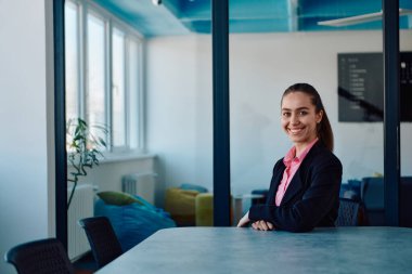 Pembe gömlekli başarılı bir bayan lider modern cam bir ofiste oturmuş kararlı bir gülümsemeyle bekliyor.