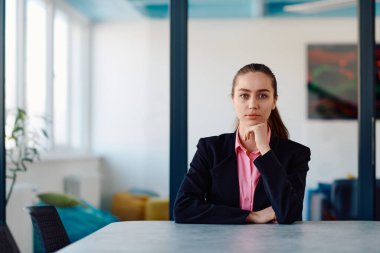 Pembe gömlekli başarılı bir bayan lider modern cam bir ofiste oturmuş kararlı bir gülümsemeyle bekliyor.