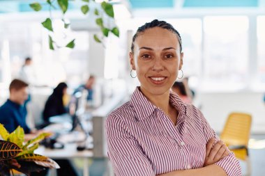 Gencecik gülümseyen iş kadınının portresi. Yaratıcı açık mekan ortak çalışma ofisinde. Başarı sahibi iş kadını, kopyalama alanı ile ofiste duruyor. Arka planda çalışan iş arkadaşları. 