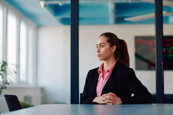 stock image Successful young female leader in a suit with a pink shirt sitting in a modern glass office with a determined smile