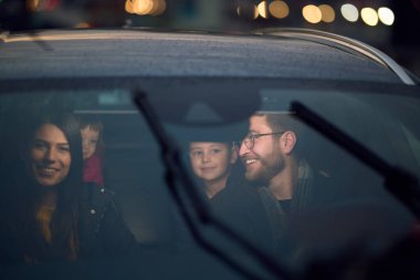 In the nighttime hours, a happy family enjoys playful moments together inside a car as they journey on a nocturnal road trip, illuminated by the glow of headlights and filled with laughter and joy. clipart