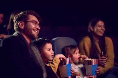 Modern bir aile, çocuklarıyla film izlerken patlamış mısırın tadını çıkarır..