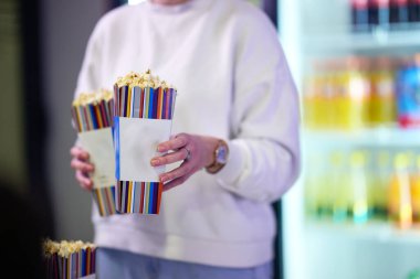 A vendor stands outside the cinema, holding freshly popped popcorn to sell to moviegoers before they enter the theater. clipart