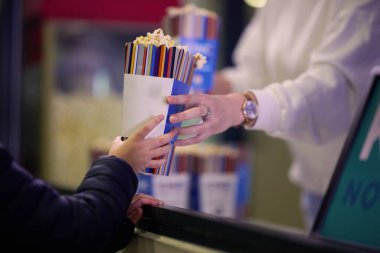 A vendor stands outside the cinema, holding freshly popped popcorn to sell to moviegoers before they enter the theater. clipart