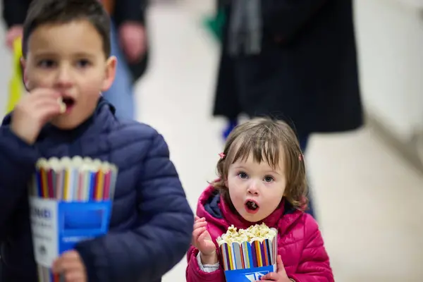 stock image A brother and his younger sister joyfully share a bag of popcorn as they head to the cinema together to watch a movie, embodying the warmth of sibling bond and anticipation for the film ahead.