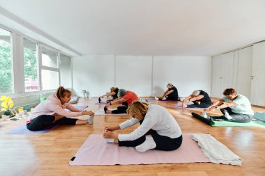 Bir grup son sınıf öğrencisi, güneş alan bir alanda eğitmenin rehberliğinde boyun, sırt ve bacak esnetme gibi çeşitli yoga egzersizleri yaparak refahı ve uyumu sağlıyorlar.. 