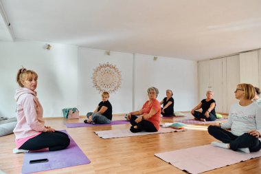 Bir grup son sınıf öğrencisi, güneş alan bir alanda eğitmenin rehberliğinde boyun, sırt ve bacak esnetme gibi çeşitli yoga egzersizleri yaparak refahı ve uyumu sağlıyorlar.. 