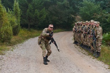 Seçkin birliğine kesin askeri talimatlar veriyor. Stratejik liderliği somutlaştırıyor. Taktik manevralar ve disiplin koordinasyonu hakkında brifing için toplanıyorlar.. 