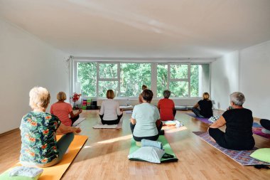 Bir grup son sınıf öğrencisi, güneş alan bir alanda eğitmenin rehberliğinde boyun, sırt ve bacak esnetme gibi çeşitli yoga egzersizleri yaparak refahı ve uyumu sağlıyorlar.. 