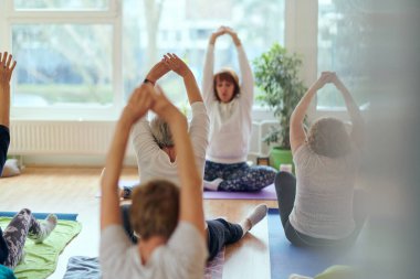 Bir grup son sınıf öğrencisi, güneş alan bir alanda eğitmenin rehberliğinde boyun, sırt ve bacak esnetme gibi çeşitli yoga egzersizleri yaparak refahı ve uyumu sağlıyorlar.. 