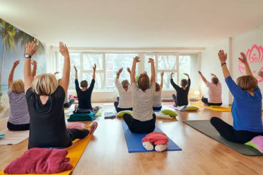 Bir grup son sınıf öğrencisi, güneş alan bir alanda eğitmenin rehberliğinde boyun, sırt ve bacak esnetme gibi çeşitli yoga egzersizleri yaparak refahı ve uyumu sağlıyorlar.. 