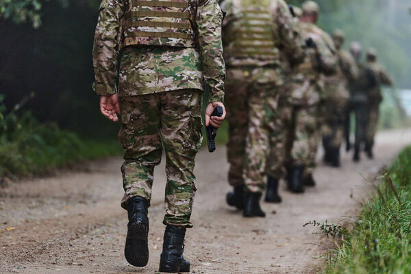 Close up photo, the resilient legs of elite soldiers, clad in camouflage boots, stride purposefully along a hazardous forest path as they embark on a high-stakes military mission. 