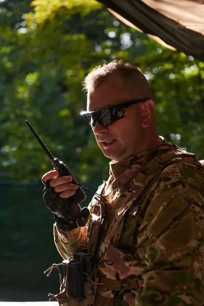 軍事大手は 戦術作戦中に仲間の兵士とのシームレスなコミュニケーションのためにモトローラララジオを使用し プロフェッショナリズムと戦略的な調整を示しています — ストック写真