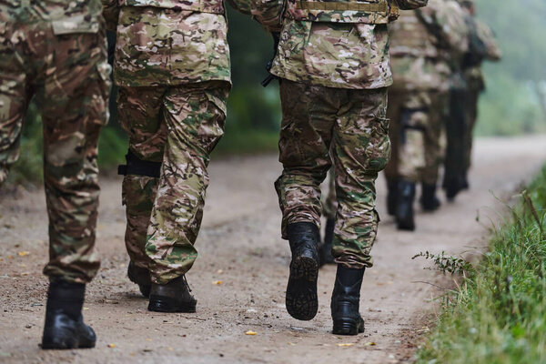 Close up photo, the resilient legs of elite soldiers, clad in camouflage boots, stride purposefully along a hazardous forest path as they embark on a high-stakes military mission. 