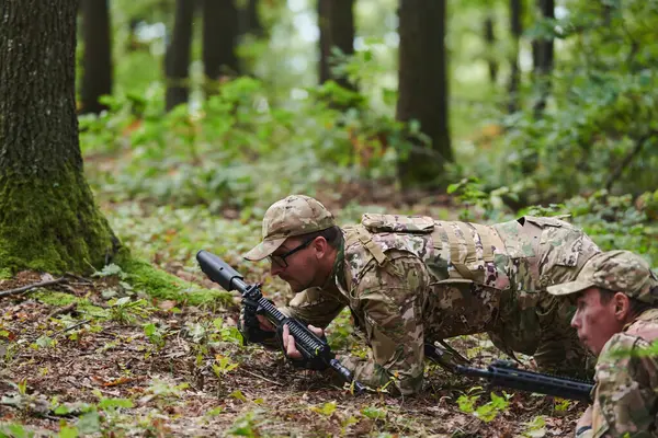 stock image Elite soldiers stealthily maneuver through the dense forest, camouflaged in specialized gear, as they embark on a covert and strategic military mission. 