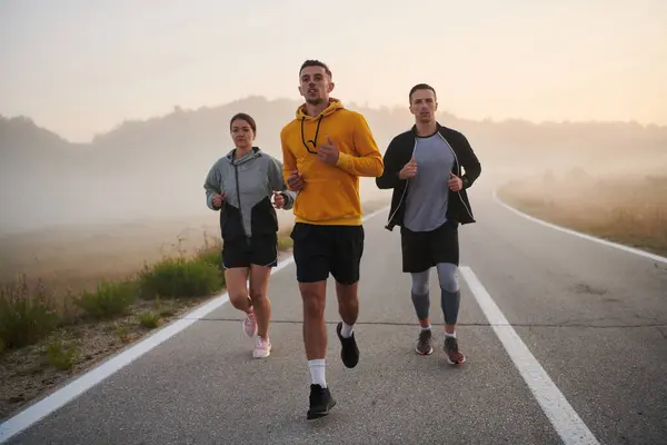 A group of sports colleagues huddle together for a pre-dawn run, the foggy air and early morning light creating an atmosphere of camaraderie and determination.