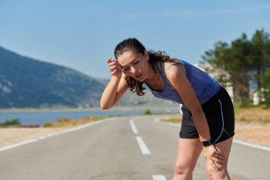 Bir kadın sporcunun dinlenirken, yoğun bir koşunun ardından terleyerek, azim ve kondisyonuna olan bağlılığını somutlaştıran, kendini adamış bir kadın sporcunun nadide görüntüsünü yakına çekiyoruz.