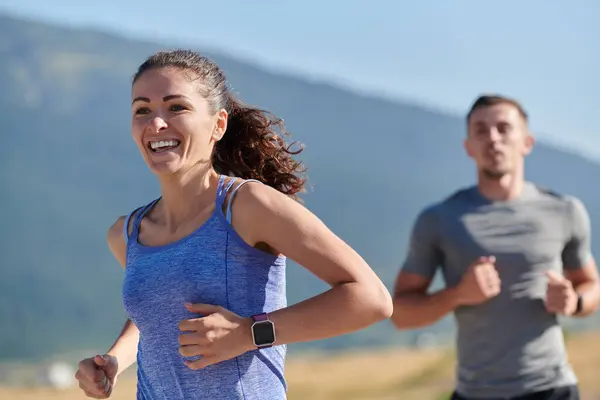 Stock image A couple runs through a sun-dappled road, their bodies strong and healthy, their love for each other and the outdoors evident in every stride. 