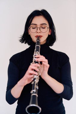 Yetenekli bir esmer müzisyen sanatını sergiliyor. Klarneti zarif bir şekilde tutuyor ve el değmemiş beyaz bir arka plana karşı çalıyor.
