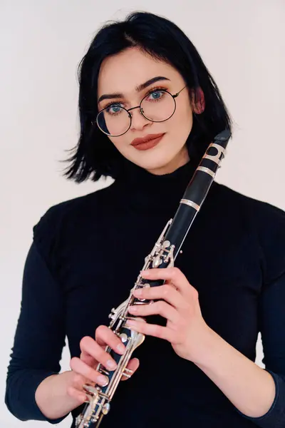 一位才华横溢的黑发音乐家优雅地拿起单簧管 在原始的白色背景下演奏 展现了她的艺术才华 — 图库照片