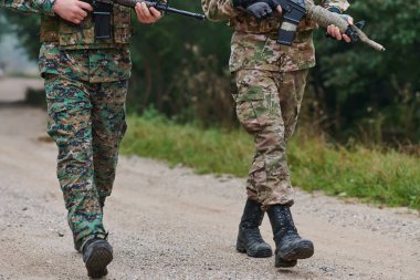 Close up photo, the resilient legs of elite soldiers, clad in camouflage boots, stride purposefully along a hazardous forest path as they embark on a high-stakes military mission.  clipart