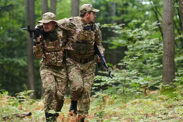 Stock image Elite soldier displays unwavering camaraderie and compassion as he aids his injured comrade, skillfully extracting him from the forest with a stretcher, showcasing the profound bond and selflessness