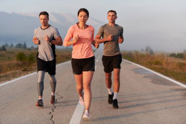 Bir grup arkadaş, sporcu ve koşucu sabahın erken saatlerinde güneşin doğuşuyla enerji dolu ve doğanın sakin güzelliğiyle çevrelenmiş bir şekilde puslu şafakta koşarken kucaklaşıyorlar..