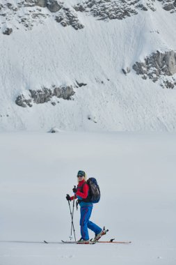A determined skier scales a snow-capped peak in the Alps, carrying backcountry gear for an epic descent clipart