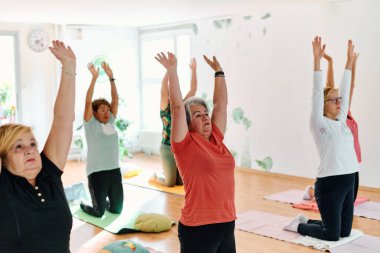 Bir grup son sınıf öğrencisi, güneş alan bir alanda eğitmenin rehberliğinde boyun, sırt ve bacak esnetme gibi çeşitli yoga egzersizleri yaparak refahı ve uyumu sağlıyorlar.. 