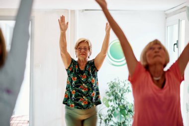 Bir grup son sınıf öğrencisi, güneş alan bir alanda eğitmenin rehberliğinde boyun, sırt ve bacak esnetme gibi çeşitli yoga egzersizleri yaparak refahı ve uyumu sağlıyorlar.. 