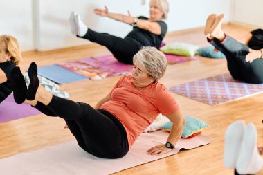 Bir grup son sınıf öğrencisi, güneş alan bir alanda eğitmenin rehberliğinde boyun, sırt ve bacak esnetme gibi çeşitli yoga egzersizleri yaparak refahı ve uyumu sağlıyorlar.. 