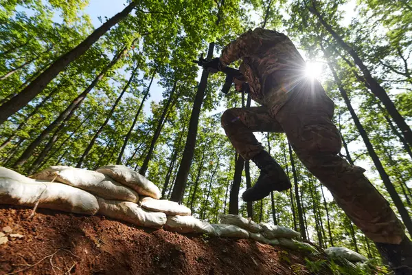 エリート兵士は 危険な森林地帯の軍事的障壁を巧みにクリアし 専門的な訓練中に戦術的なスキルと敏捷性を示しています ロイヤリティフリーのストック画像