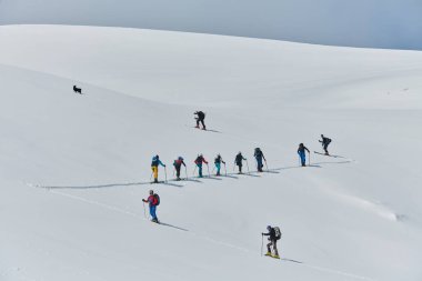 A group of professional ski mountaineers ascend a dangerous snowy peak using state-of-the-art equipment.  clipart