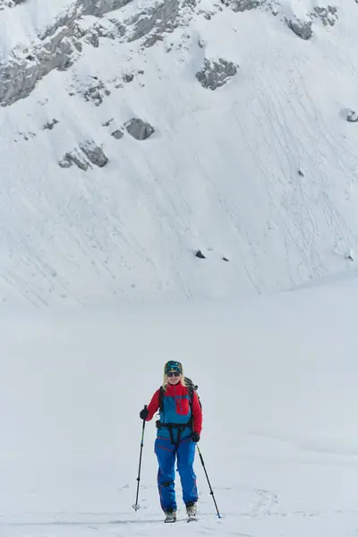決められたスキーヤーはアルプスの雪に覆われたピークをスケールし 壮大な降下のためのバックカントリーギアを運ぶ — ストック写真