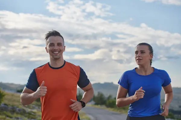 スポーツウェアを着たカップルは 早朝のトレーニング中に美しい道に沿って走り 新鮮な空気を楽しみ 健康的なライフスタイルを維持します ロイヤリティフリーのストック画像