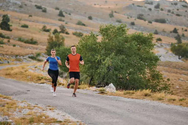 一对穿着运动服的夫妇在晨练时沿着风景秀丽的道路跑步 享受新鲜空气 保持健康的生活方式 免版税图库照片